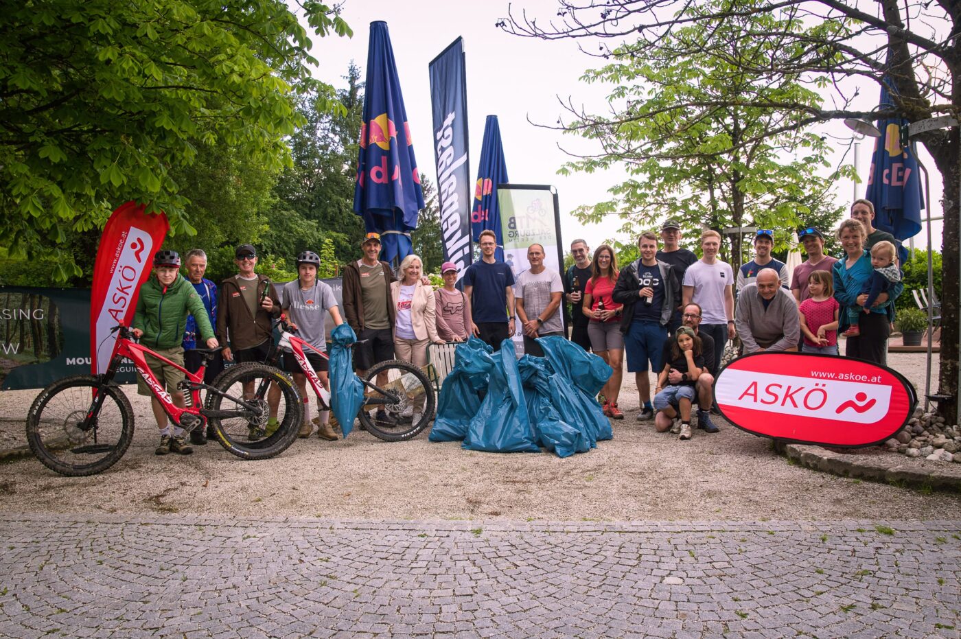 Eine Gruppe Mountainbiker mit aufgestapelten, gefüllten Müllsäcken, die vor ihnen liegen.