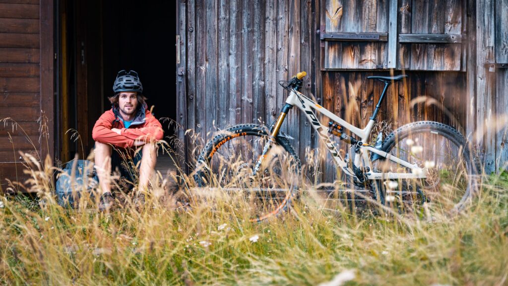 Ein Mountainbiker mit seinem Enduro vor einer Hütte.